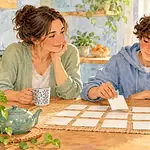 Teenager choosing blank revision cards while a caregiver follows calmly at a kitchen table