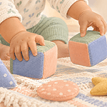 A baby explores soft cubes and stacking cups with both hands