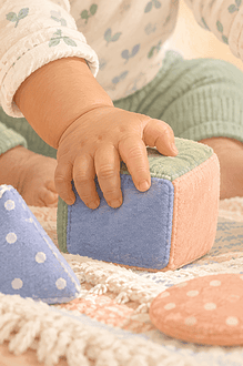 A baby explores soft cubes and stacking cups with both hands