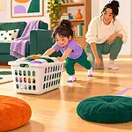 Child safely pushing a laundry basket along a clear indoor route while a caregiver supervises